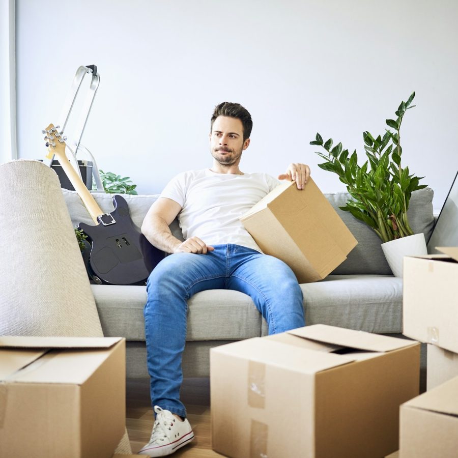 Frustrated man sitting on couch surrounded by cardboard boxes